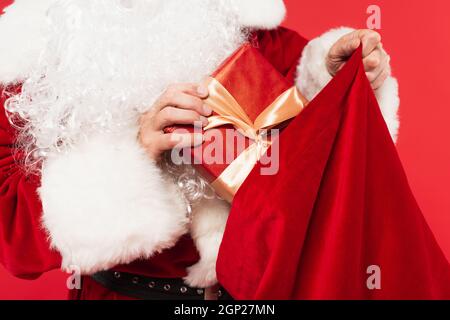 Vista croppata di babbo natale mettere dono in sacco isolato su rosso Foto Stock