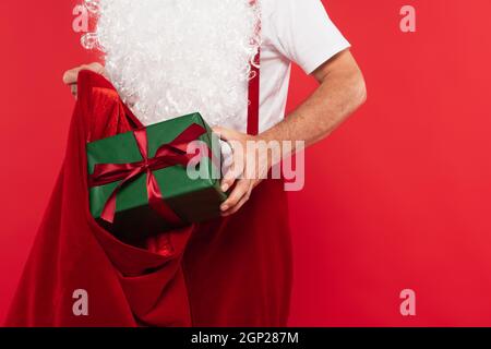 Vista ritagliata di babbo natale mettendo presente in sacco isolato su rosso Foto Stock