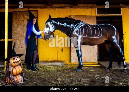 Una ragazza vestita come strega ha preso un cavallo fuori di un corale con uno scheletro dipinto in vernice bianca Foto Stock