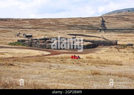 Villaggio Maasai, recinzione compatta, piccole case rotonde, tetti di paglia, gente recinzione esterna, abbigliamento tradizionale rosso, gruppi semi-nomadi tribù, collina Foto Stock