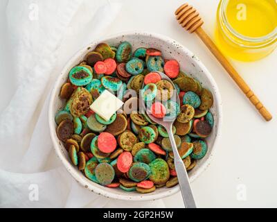 Cibo alla moda - cereali pancake. Un mucchio di mini frittelle di cereali colorate. Minuscoli pancake di colore naturale: Matcha verde, spirulina turchese, pisello blu, re Foto Stock