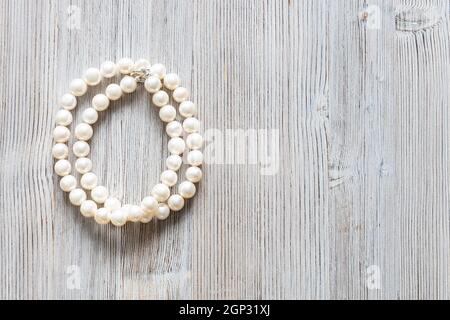 collana piegata in madreperla bianca naturale su sfondo grigio di legno con copyspace Foto Stock