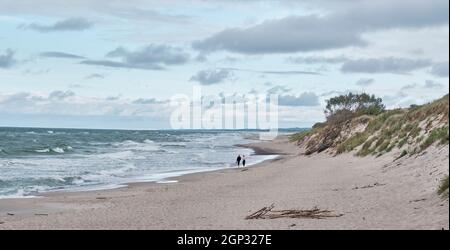 Bella vista mare con onde, spiaggia sabbiosa e cielo nuvoloso. Coppia camminando lungo il bordo dell'acqua. Foto Stock