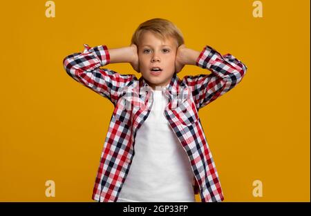 Sconvolto emotivo ragazzo europeo studente ragazzo copre le orecchie con le mani, non vuole ascoltare, isolato su sfondo giallo, copia spazio, studio shot. Str Foto Stock