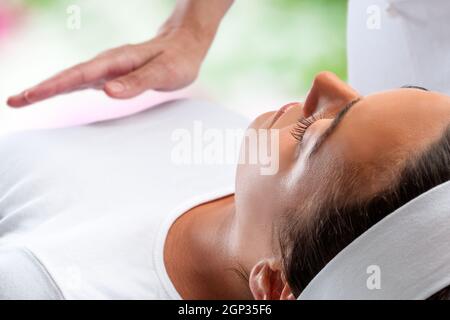 Close up ritratto di giovane donna in un momento di relax a sessione di reiki con terapista mano in background. Foto Stock