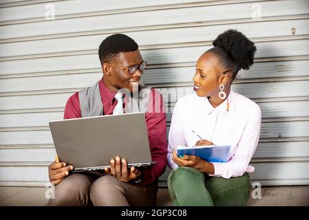 coppia africana d'affari seduta e di lavoro con un cellulare mentre sorride. donna che prende nota nel suo documento Foto Stock
