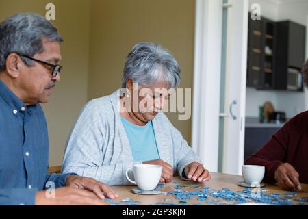 Due diversi amici maschili e femminili seduti a tavola e facendo puzzle Foto Stock