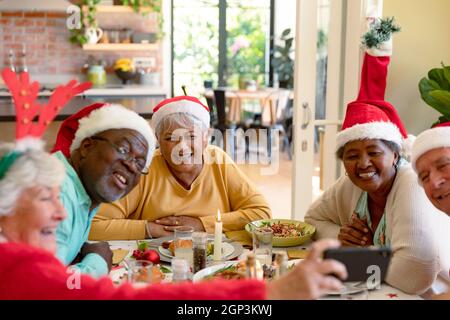 Gruppo vario di amici anziani felici in cappelli di festa che celebrano il natale insieme, prendendo selfie Foto Stock