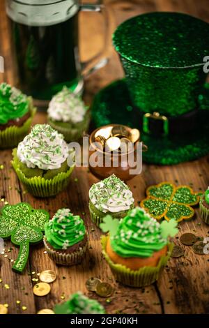 Concetto di giorno di San Patrizio con pentola d'oro, shamrock e cupcakes su sfondo di legno. Foto Stock