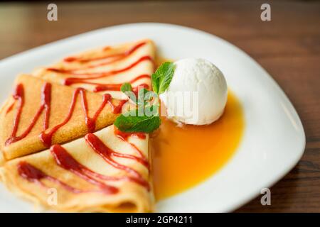 alcuni pancake da dessert con marmellata di fragole, miele e un cucchiaio bianco di gelato. Concetto - menu per un caffè Foto Stock