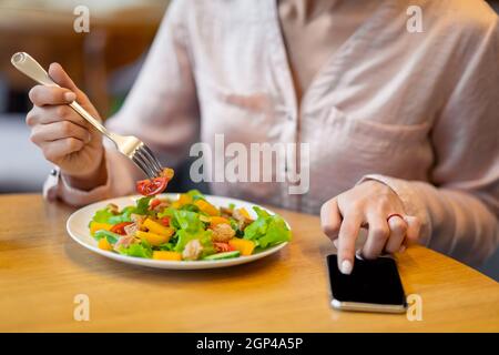 Calcolo delle calorie e concetto di controllo degli alimenti. Donna che usa lo smartphone con schermo nero e mangiare insalata fresca, seduto in un bar e utilizzando l'applicazione su Foto Stock