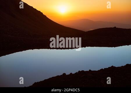 Splendido scenario di grande lago e silhouette di montagne al tramonto bagliore luce nelle montagne di Tien Shan, Kazakistan. Foto Stock
