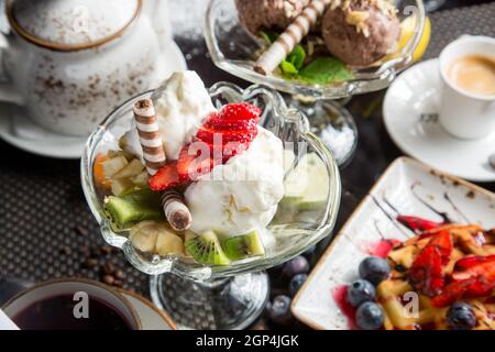 Dessert italiano - cialde croccanti con gelato, formaggio cremoso e marmellata. Pezzi di frutta per dessert. Concetto - alimento dolce, problema di obesità. Foto Stock