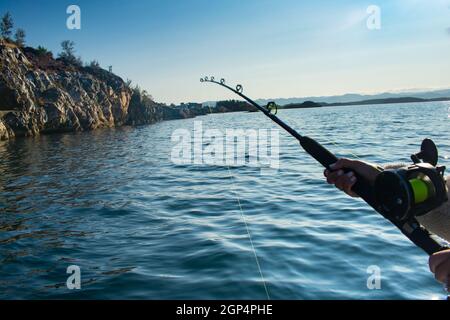 La canna da pesca e la mulinello si trovano a distanza da una barca sull'oceano a Stavanger, Norvegia Foto Stock