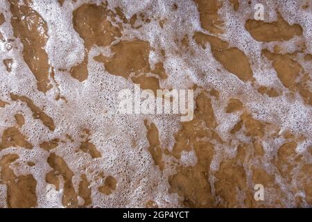 Lacy modello di onda e schiuma di mare che rotola sulla riva. Foto Stock