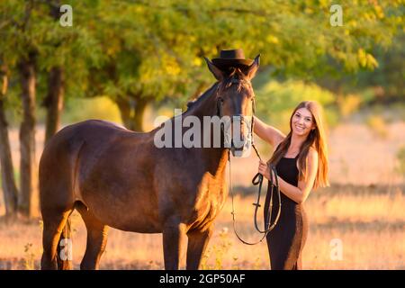 La ragazza ha messo su un cappello su un cavallo per una passeggiata e  ammira il cavallo Foto stock - Alamy