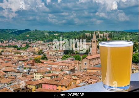 Bicchiere di birra leggera sul tavolo con vista sul centro della città con tetti rossi a Verona, Italia. Vista dall'alto del centro storico di Verona. Foto Stock