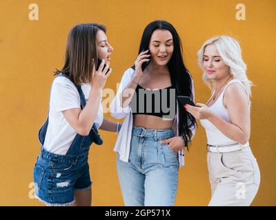 Tre giovani amiche che usano i loro telefoni cellulari mentre trascorrono del tempo insieme. Foto Stock