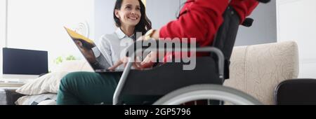 Donna in sedia a rotelle con computer portatile comunica con un amico Foto Stock