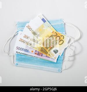 maschera igienica monouso e banconote in euro su sfondo grigio Foto Stock