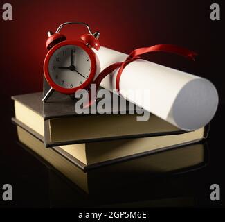 Un diploma in cima a una coppia di libri mostra il successo di profitto degli studi scolastici, mentre un orologio sveglia ci ricorda l'importante calendario a portata di mano. Foto Stock