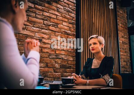 Una bionda attraente con rossetto rosso che spiega la sua strategia per un incontro d'affari in un ristorante Foto Stock