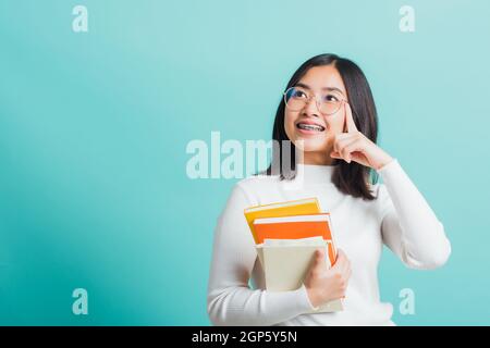 Ritratto femmina in occhiali sta tenendo i libri a portata di mano, giovane bella donna asiatica hugging libri, studio girato isolato su uno sfondo blu, educati Foto Stock