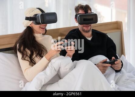 Coppia felice indossando un visore per realtà virtuale e divertendosi mentre giocate insieme ai videogame VR a letto . Concetto di gaming e tecnologia Foto Stock