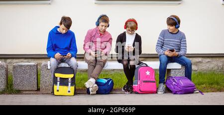 Bambini con zaini seduti sulla panca del parco vicino alla scuola. Relazioni umane. Giovani generazioni. Foto Stock