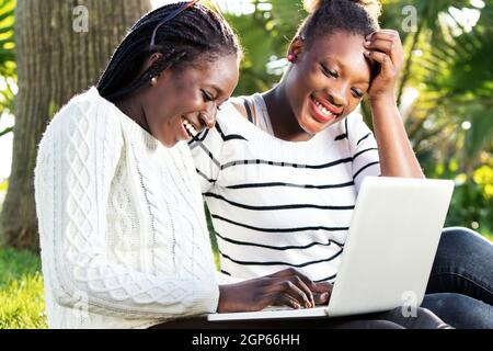 Primo piano ritratto all'aperto di due ragazze teen americane afro socializzare su laptop in parco. Foto Stock