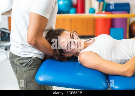Mani dell'uomo che fanno il collo di articolazione manuale che si allunga e che danno un massaggio del collo ad una giovane donna caucasica Foto Stock