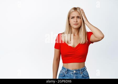 Confusa ragazza grattando testa, guardando perplesso a qualcosa di strano, non capire, in piedi su sfondo bianco Foto Stock