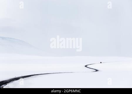Incredibile paesaggio invernale. Strada vuota tra i campi ricoperti di neve. Sfondo bianco grigio naturale. Tempesta tempo dell'Islanda. Foto Stock