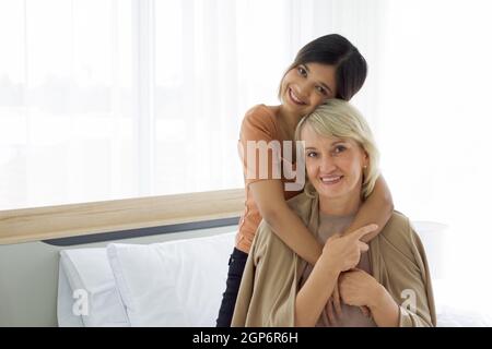 Happy mix pelle famiglia vivere insieme, figlia asiatica e adottato cuddle madre caucasica a vicenda con sorrisi. Concetto di amore e di condivisione del tempo Foto Stock