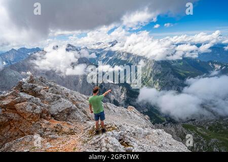 L'escursionista punta in lontananza, sulla cima del Partenkirchner Dreitorspitze, vista nella valle di Reintal verso le cime coperte di nuvole Foto Stock