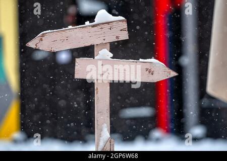 cartello in legno innevato con due frecce nlank su un colorato sfondo sfocato Foto Stock