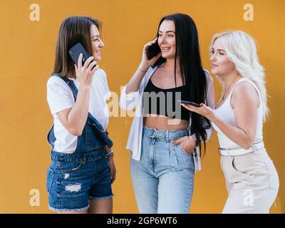 Tre amici femminili che usano i loro moderni telefoni cellulari mentre si divertono insieme all'aperto. Foto Stock