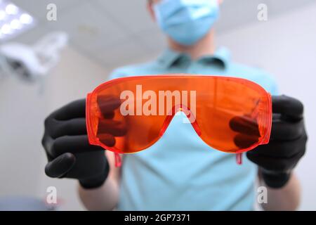 Occhiali di sicurezza arancioni nelle mani di un dentista. Foto irriconoscibile. Spazio di copia. Foto Stock