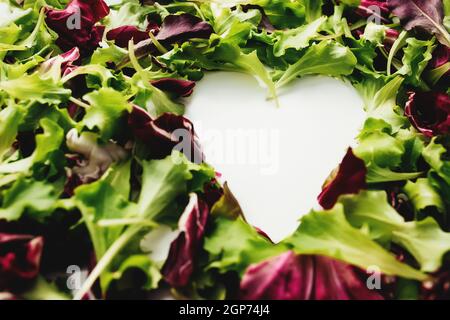 Forma del cuore da foglie di insalata verde e viola mescolano lo sfondo. Tavola bianca. Foto di alta qualità Foto Stock