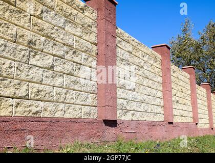 Recinzione fatta di mattoni e intonaco decorativo. Recinzione di colore giallo con elementi di colore rosso. Alta e bella scherma. Foto Stock