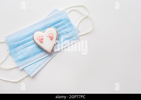 Maschera medica monouso e due cuori. Cuore con footprint del bambino. Parto nella pandemia del coronavirus Foto Stock