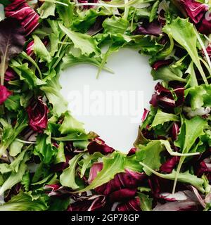 Forma del cuore da foglie di insalata verde e viola mescolano lo sfondo. Tavola bianca. Foto di alta qualità Foto Stock