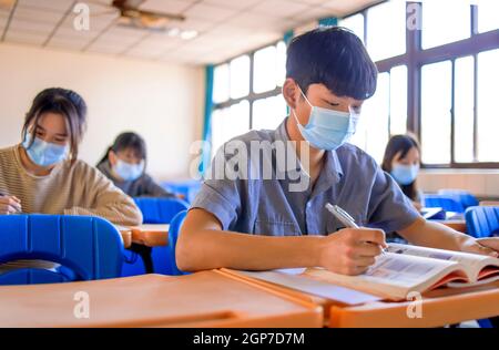 Gruppo di studenti che indossano maschere di protezione e studiano in classe Foto Stock