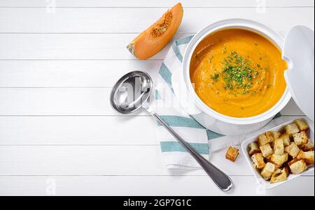 Zuppa di zucca in ciotola di ceramica, con crostini e erba cipollina su sfondo bianco in legno, vista dall'alto, spazio copia. Foto Stock