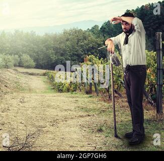 Stanco agricoltore nella vigna poggiando su la zappa Foto Stock