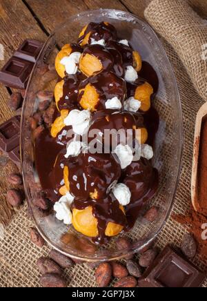 Profitteroles al cioccolato con crema di cacao in polvere, le fave di cacao e pezzi di cioccolato. Foto Stock