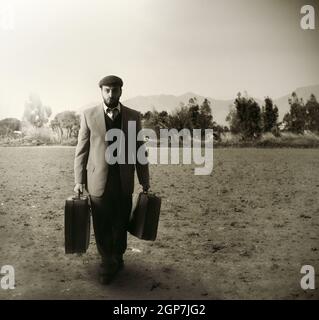 Emigrante uomo con le valigie in un campo agricolo Foto Stock