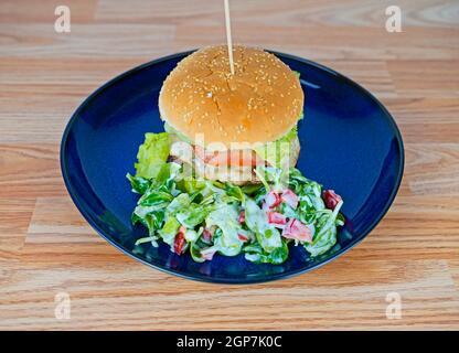 Cheeseburger con contorno di lattuga di agnello servito su piatto blu Foto Stock