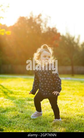 Piccola bambina gioca felice nel parco all'aperto nella primavera in controluce. Foto Stock