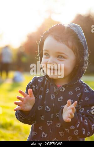 Piccola bambina gioca felice nel parco all'aperto nella primavera in controluce. Foto Stock